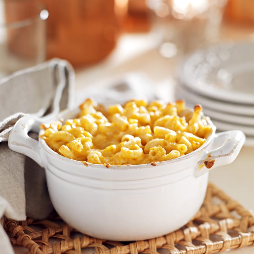 A white ceramic bowl filled with golden-brown baked macaroni and cheese on a woven placemat.