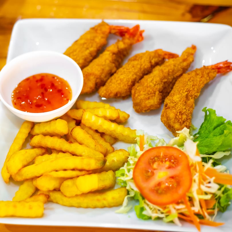 Fried shrimp, french fries, sweet chili sauce, and a side salad on a white plate.