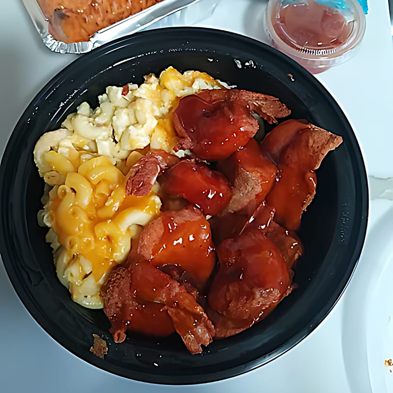Soul food bowl with macaroni and cheese, and sliced hot dogs covered in BBQ sauce.